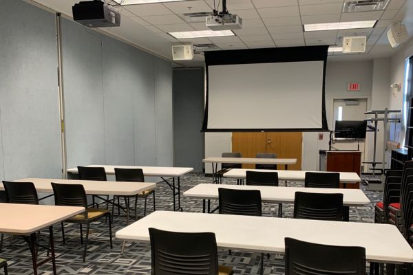 Room B with tables arranged in rows with chairs on one side facing front of room; up to 16 people at 8 tables (plus presenter or panel).