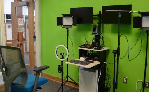 A video recording room (in green screen color) with a computer, video camera, microphones, and lighting