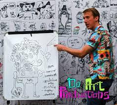 Light-skinned man in a colorful shirt, standing in front of a background of comic-style drawings, while drawing on a flip chart. Text: Do Art Productions