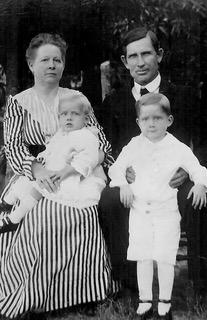 A family of four in a black and white photo in old fashioned clothing