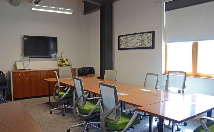 The Board Room has eight chairs around four tables and a large monitor.