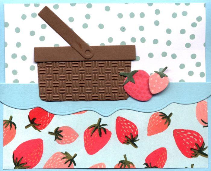 A greeting card with a picnic basket and a scattering of strawberries