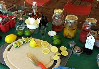 A cutting board with lemons and limes cut in slices and various herbs in jars