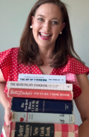 Presenter Leslie Goddard smiles as she holds a stack of cookbooks
