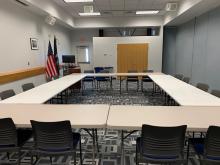 Room A with tables arranged in large square with chairs around outside edge; up to 16 people.