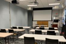 Room B with tables arranged in rows with chairs on one side facing front of room; up to 16 people at 8 tables (plus presenter or panel).